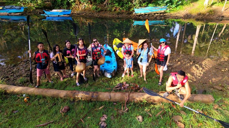 A happy group of kayakers in life vests gathered at the river bank with colorful kayaks